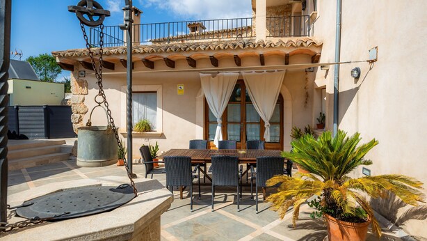A patio with a table and chairs, a potted plant, and a stone structure.