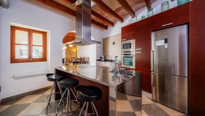 A modern kitchen with a central island, bar stools, stainless steel appliances, and wooden ceiling beams.