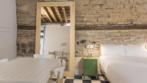 A room with a stone wall, a bed, a green nightstand, a white table, and a chair. - La Casa de la Tuerta   El Rincón de Éboli (Toledo)