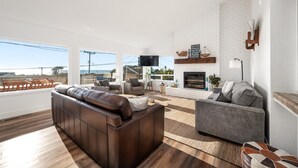 A modern living room with a fireplace, leather sofa, and a view of the city. - Ocean Views-Fire Pit-Walk to Beach (Cayucos)