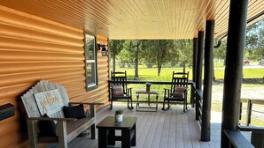 Eine überdachte Veranda mit Holzboden, einer Bank, einem Tisch mit einer Pflanze und Blick auf eine Rasenfläche.