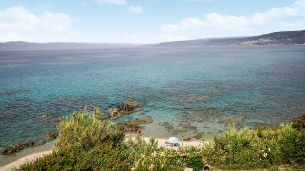 Een kustgezicht met helder turquoise water, rotsachtige rotsformaties en weelderige begroeiing.