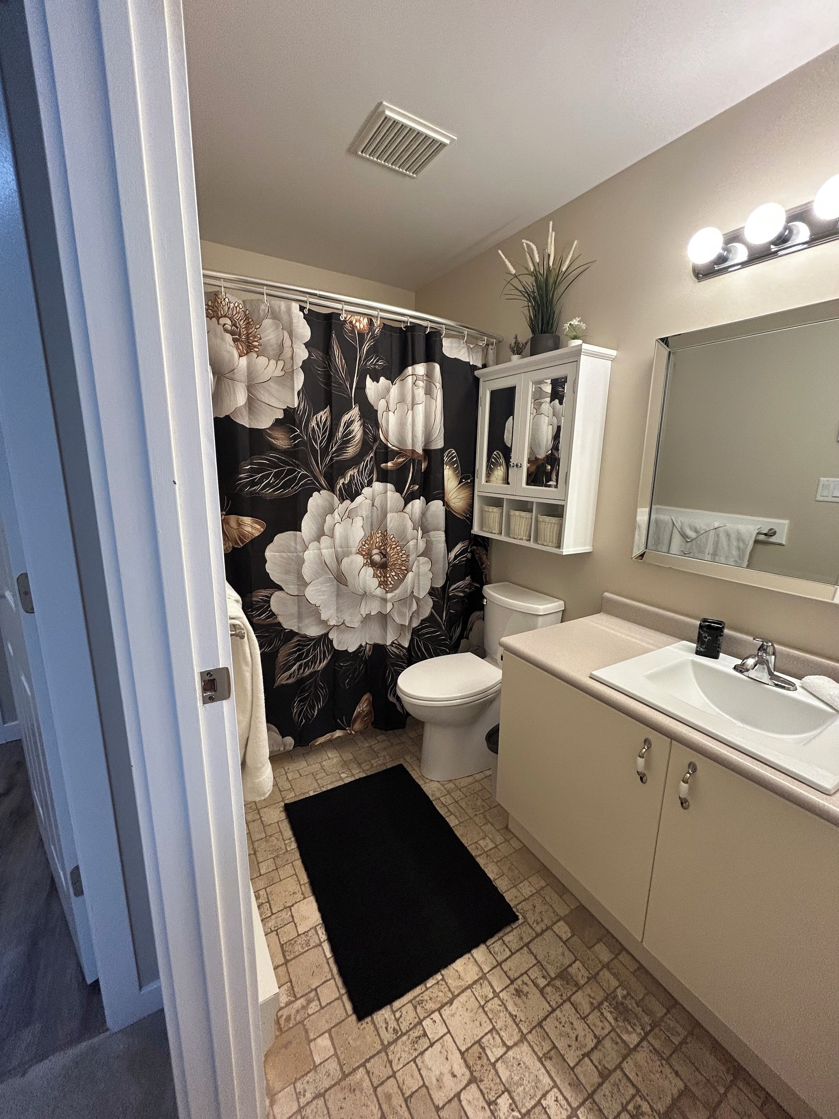 A bathroom with a toilet, sink, mirror, and shower curtain with a floral pattern.