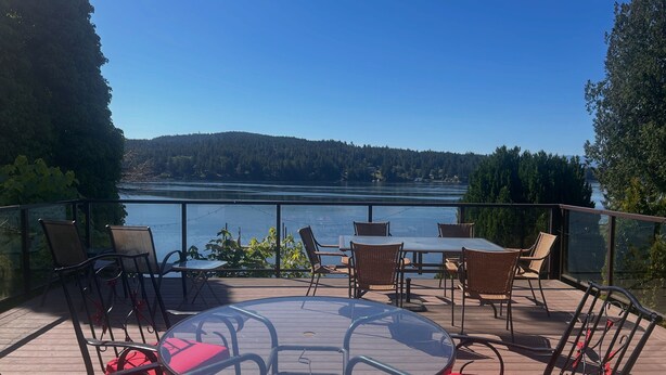 Eine Terrasse mit einem Glastisch und Stühlen, mit Blick auf einen See und bewaldete Hügel.