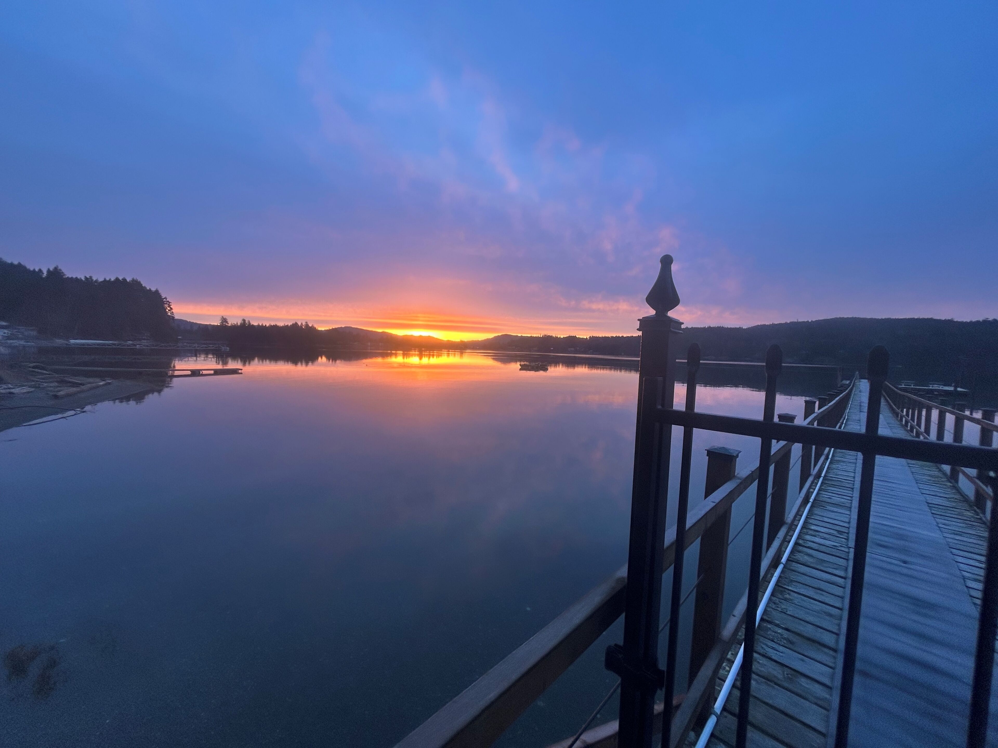 A calm lake at sunset with a wooden dock extending into the water.