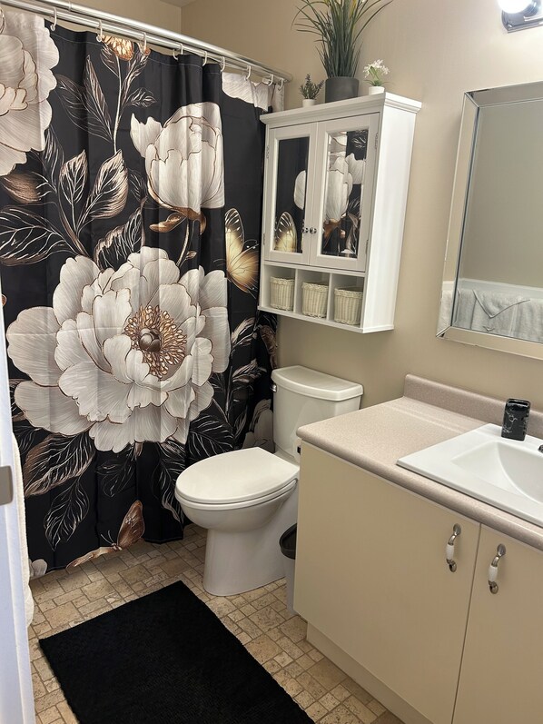 A bathroom with a toilet, a sink, a cabinet, and a shower curtain with a floral pattern.