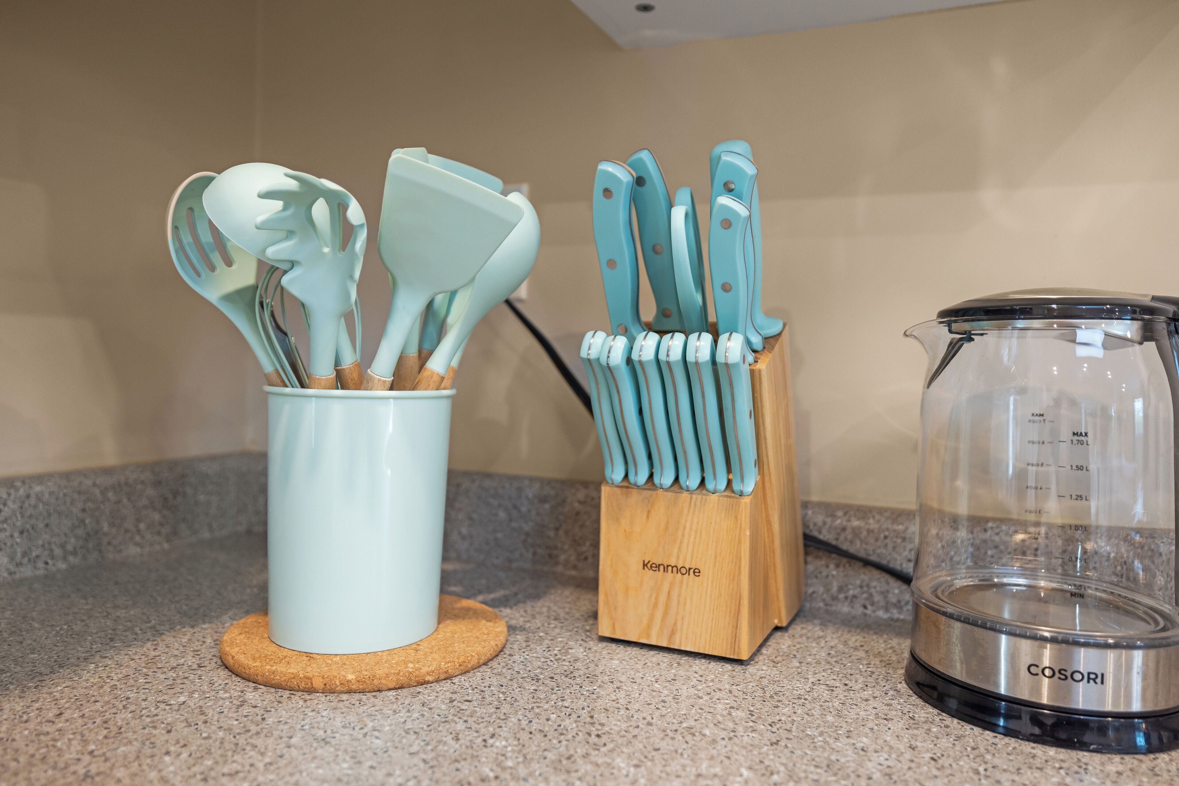 Un plan de travail de cuisine avec une tasse blanche, un porte-ustensiles en bois contenant des couteaux à manche bleu et un récipient en verre transparent muni de graduations.