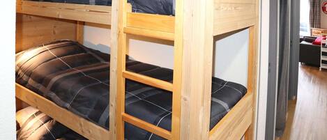Una cama litera de tres niveles, estructura de madera y ropa de cama negra.