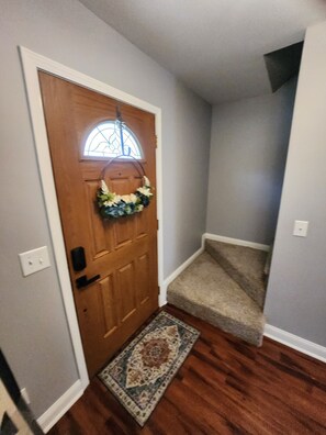 Une porte en bois avec un panneau de verre et une guirlande, qui donne sur un escalier recouvert de moquette.