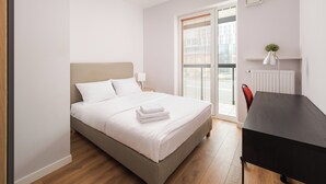 A neatly made bed with white linens, a bedside table with a lamp, and a view of the outside through a sliding glass door.