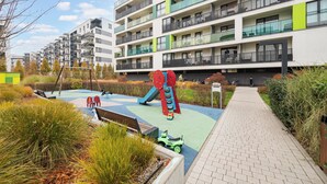 A playground with slides and swings, surrounded by a landscaped garden and a multi-story residential building with balconies.