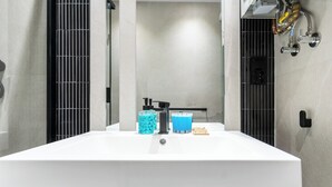 Une salle de bain moderne avec un grand lavabo blanc, des accessoires noirs et une cloison en verre.