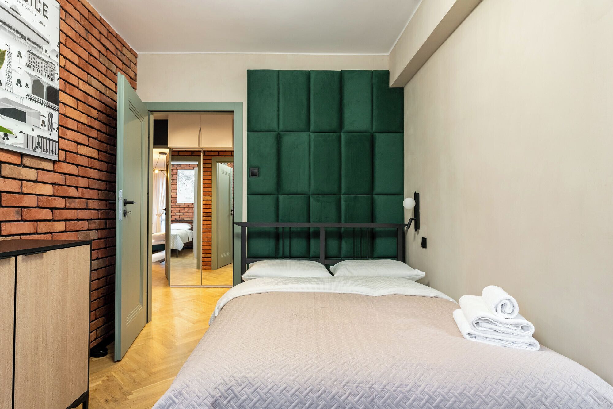 Une chambre d’hôtel avec un lit, une tête de lit recouverte d’un tissu vert, une armoire en bois et un miroir.