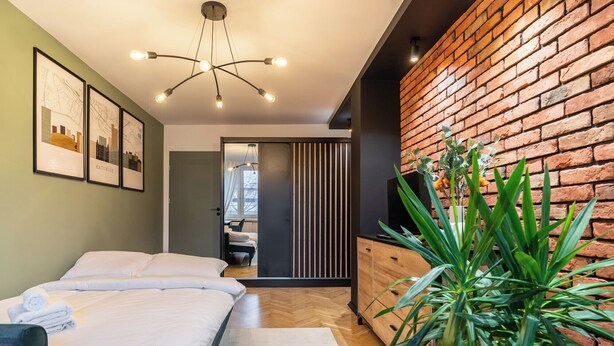 Une chambre d’hôtel moderne avec deux lits, un plancher en bois, un mur décoratif en briques et une grande plante verte.