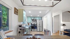 Una cocina moderna con electrodomésticos de acero inoxidable, un comedor con mesa de madera y vistas al bosque a través de un ventanal grande.