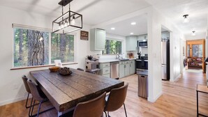 Una cocina moderna con una mesa de comedor de madera, ventanas amplias y vistas al bosque.