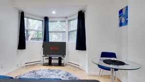 Un salón moderno con un televisor de pantalla plana, una mesa de vidrio y una silla azul.