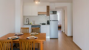 Eine moderne Küche mit weißen Schränken, einer Mikrowelle und einem Kühlschrank. Ein Esstisch mit Stühlen und eine Deckenleuchte sind ebenfalls vorhanden.