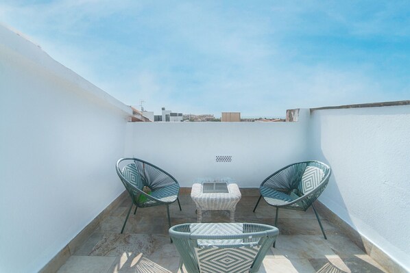 A small outdoor seating area with two chairs and a table, surrounded by white walls and a clear sky.