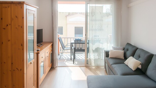 Ein modernes Wohnzimmer mit grauem Sofa, Holzschrank und einem Balkon mit Tisch und Stühlen.