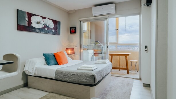 A modern bedroom with a bed, a painting, a balcony with a view, and a small table. - WELCS APARTAMENTO 190 EMP cerca del mar (Empuriabrava)