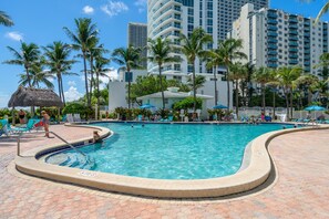 A swimming pool with a hot tub, surrounded by palm trees and lounge chairs.