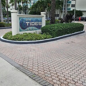 Ein Schild für das Hotel 'The Tides' mit sechseckiger Fliesenpflasterung und umliegender Bepflanzung.