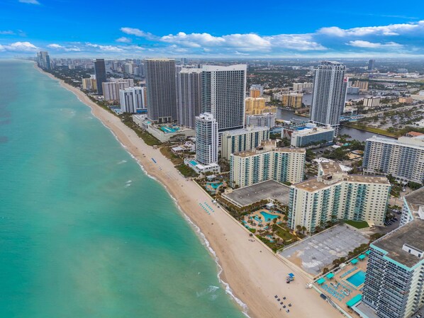 A coastal cityscape with high-rise buildings, a beach, and a marina.