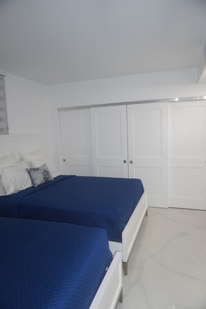 A bedroom with two beds, white walls, and a large wardrobe.