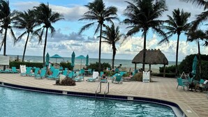 A swimming pool with lounge chairs and umbrellas, surrounded by palm trees and a view of the ocean.
