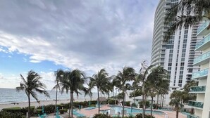 A resort pool area with palm trees, a grassy lawn, and a building with balconies.