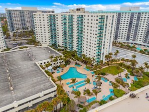 A high-rise hotel with a rooftop pool surrounded by palm trees and lounge chairs.