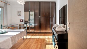Un dormitorio moderno con suelo de madera, cama con colcha blanca, armario con puertas de espejo y un banco con toallas.