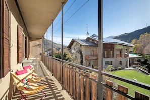 A balcony with wooden railings, a view of a mountain, and a building with a stone facade.