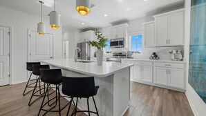 A modern kitchen with white cabinetry, a central island with bar stools, stainless steel appliances, and pendant lighting.