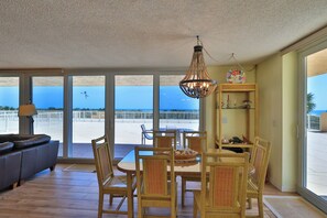 A spacious living area with a view of the ocean, a dining table with chairs, and a chandelier.