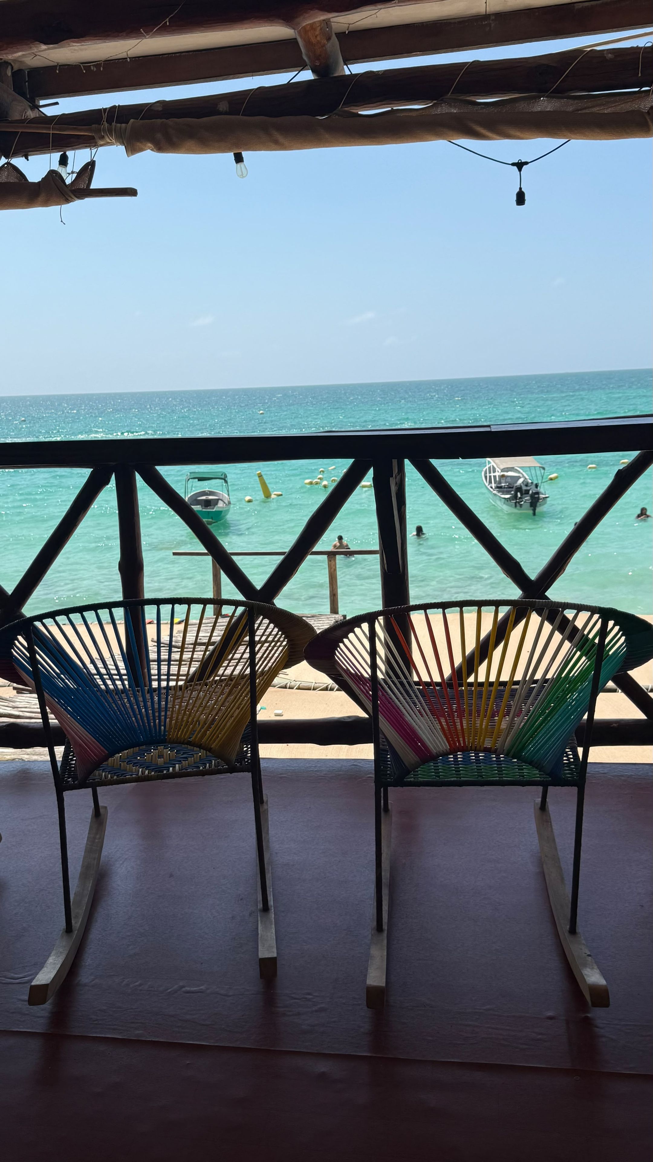 A beach view from a covered area with two colorful woven chairs.
