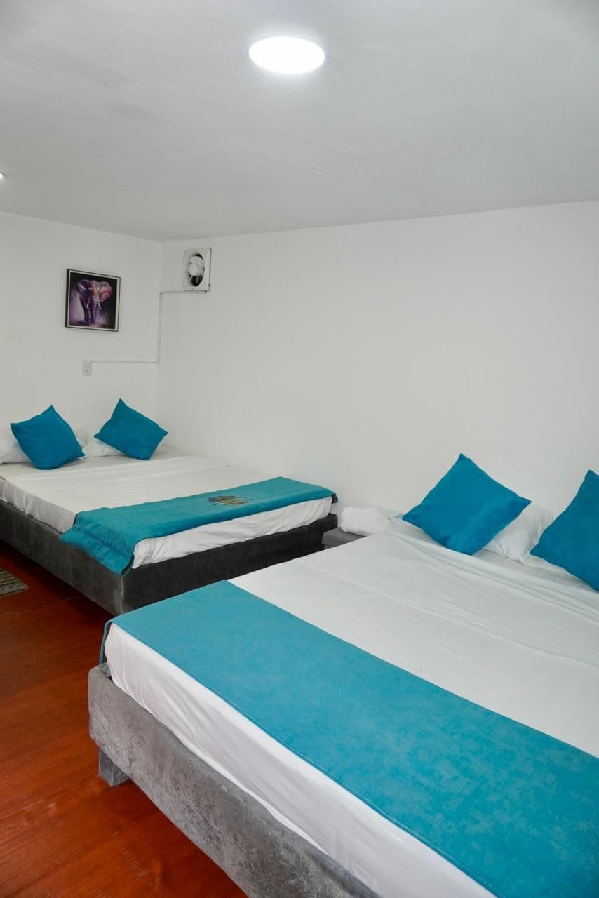 A hotel room with two beds, each with a blue bedspread and pillows, and a single bed with a similar setup.