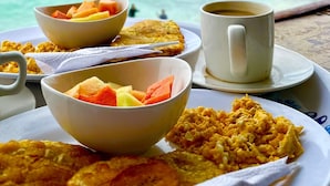 Morgenmad med havudsigt, inklusive tallerkener med røræg, ristet brød og frugt, samt en kop kaffe.