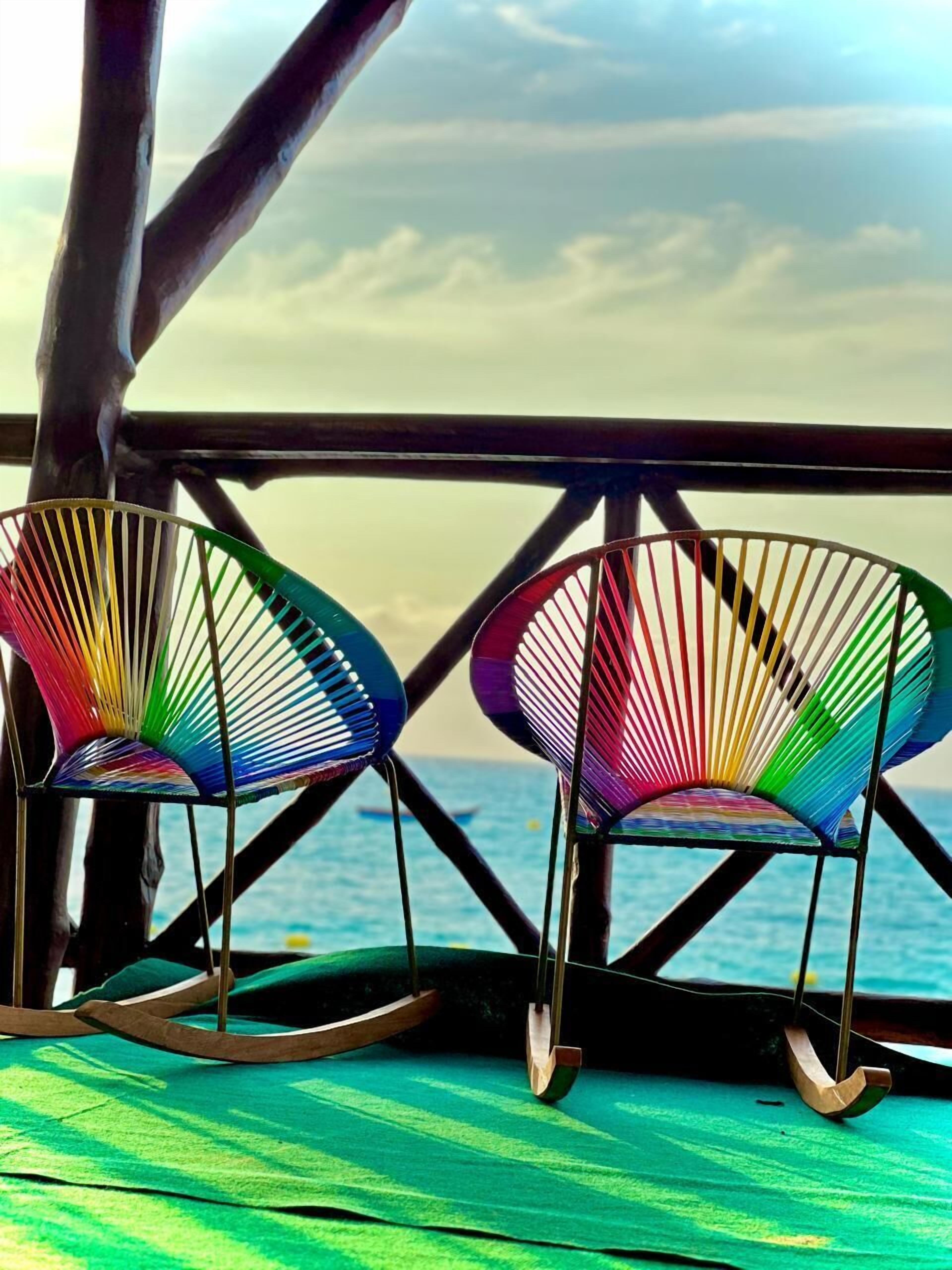 Two colorful rocking chairs on a wooden deck with a view of the sea.