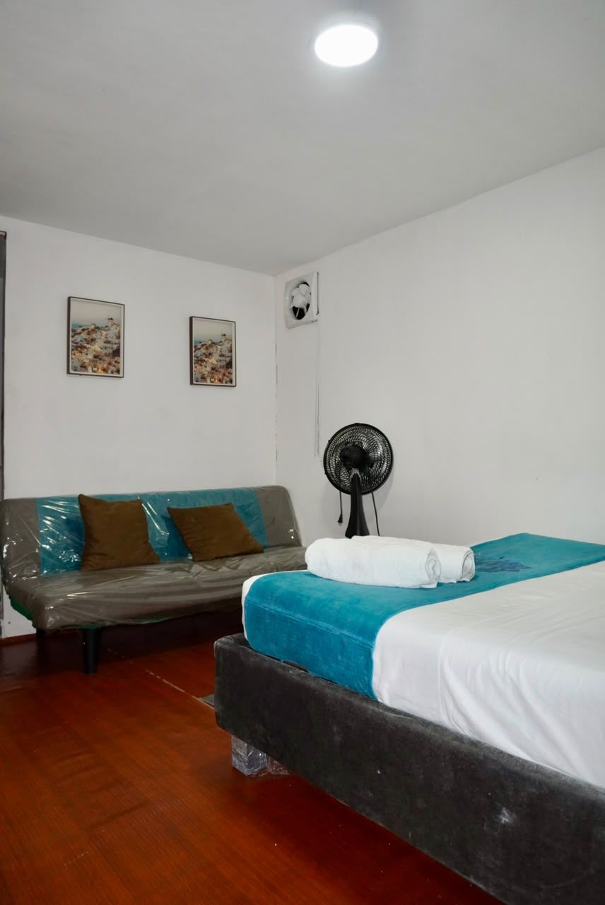 Quarto com cama, sofá, ventilador e duas quadros pendurados na parede.
