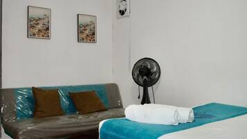 Quarto com cama, sofá, ventilador e duas quadros pendurados na parede.