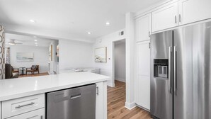 A modern kitchen with white cabinetry, stainless steel appliances, and a wooden floor. - Beachside Oasis in Newport Beach – Steps to Balboa Park, Pier, and The Fun Zone! (Newport Beach)