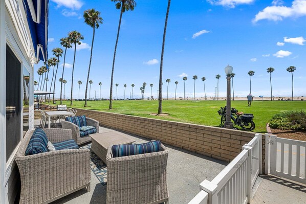A patio with wicker furniture, a view of a beach with palm trees, and a clear blue sky.