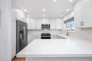 A modern kitchen with white cabinetry, stainless steel appliances, and recessed ceiling lights.