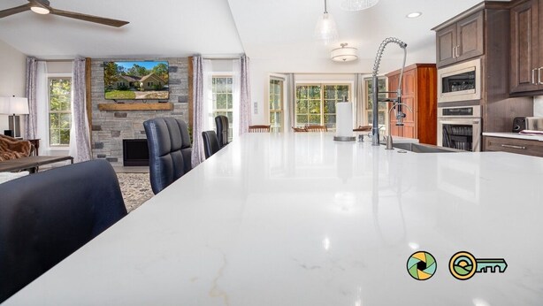 A spacious living room with a large white marble island, a stone fireplace, and a television mounted on the wall. - Pine Cone Paradise - escape to luxury! (Mount Jackson)