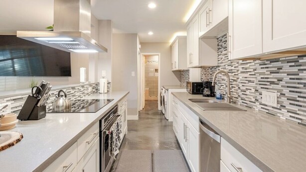 Uma cozinha moderna com armários brancos, coifa de aço inoxidável e backsplash revestido de azulejos.
