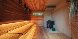 A wooden cabin interior with a bench, a fireplace, and a window. - NEGURA (Ogimi)