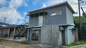A modern two-story building with a concrete facade, a small window, and a visible staircase leading to an upper level. - NEGURA (Ogimi)