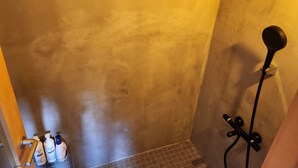 A bathroom with a shower, a towel rack, and toiletries on the wall. - NEGURA (Ogimi)